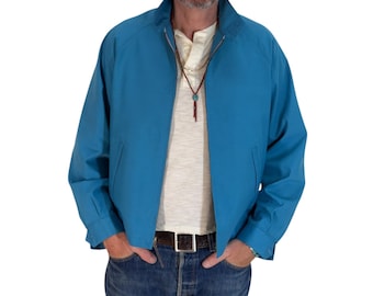 May include: A bright blue zip-up jacket with a high collar, long sleeves, and two side pockets. The jacket is worn over a cream-colored henley shirt, paired with blue denim jeans and a dark brown leather belt with a silver buckle.