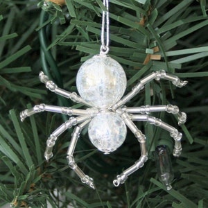 May include: A silver beaded spider Christmas ornament with clear iridescent glass beads for the body. The spider is hanging from a silver string.