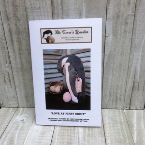May include: A black and white penguin with a pink egg, a basket of eggs, and a tag that says "Love at First Sight". This is a pattern for a primitive cloth sculpture, approximately 10 inches tall.