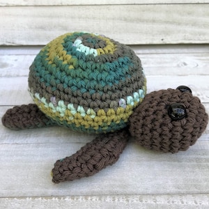 May include: A crocheted turtle toy with a green, brown, and yellow shell and brown legs. The turtle has black eyes.