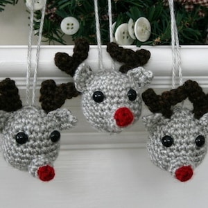 May include: Three gray crocheted reindeer ornaments with brown antlers and red noses hanging from white string.