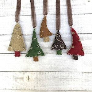 May include: Five felt Christmas tree ornaments hanging from brown ribbon. The trees are in various colors, including brown, green, red, and tan. Each tree has gold beads sewn on.