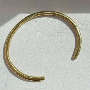 May include: A thick gold-colored metal bangle bracelet with a smooth, rounded surface.