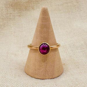 May include: A gold ring with a purple oval gemstone set in the center.
