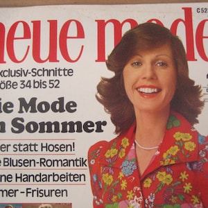 Può includere: Una copertina di rivista con una donna con lunghi capelli castani che indossa una blusa rossa con stampa floreale. La rivista è intitolata "neue mode" e il testo "Die Mode im Sommer" è anche visibile. La copertina della rivista presenta il testo "92 Exclusiv-Schnitte in Größe 34 bis 52" e "Kleider statt Hosen! Neue Blusen-Romantik Schöne Handarbeiten Sommer-Frisuren".