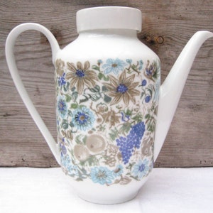 May include: White ceramic coffee pot with a floral pattern in shades of blue, brown, and green. The pot has a wide spout and a curved handle.