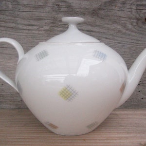 Può includere: Teiera in porcellana bianca con coperchio e manico. La teiera presenta un motivo geometrico di quadrati colorati.