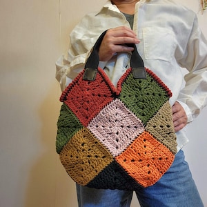 May include: A colorful, handmade crochet tote bag. The bag features a patchwork design with squares of red, green, pink, orange, brown, and black. It has black handles with leather accents and a sturdy, textured appearance.