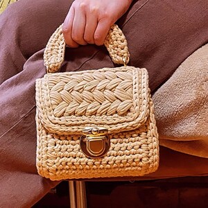 May include: A small, beige crocheted handbag with a gold clasp and top handle.