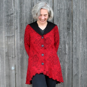 Peut inclure: Veste rouge avec col noir et trois boutons noirs. La veste présente un motif de roses et un ourlet ondulé. La personne sur l'image porte la veste.