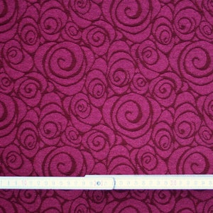 Peut inclure: Gros plan sur un tissu avec un motif de tourbillons r&eacute;p&eacute;t&eacute;s dans des tons bordeaux et marron fonc&eacute;. Une r&egrave;gle gradu&eacute;e en centim&egrave;tres est plac&eacute;e en bas, indiquant l'&eacute;chelle du motif. Le tissu pr&eacute;sente un aspect textur&eacute;.