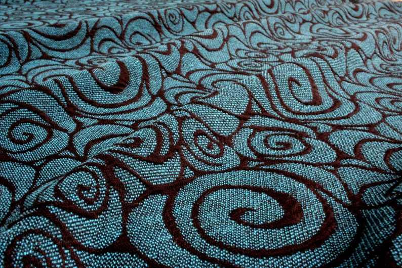 May include: Close-up of a teal blue fabric with a brown swirl pattern. The fabric has a textured, woven look.