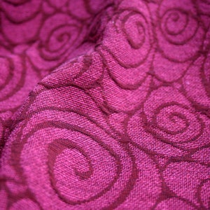 Peut inclure: Gros plan sur un tissu magenta avec un motif de tourbillons r&eacute;p&eacute;t&eacute;s dans une nuance plus fonc&eacute;e de magenta. Le tissu textur&eacute; semble &ecirc;tre tiss&eacute;, avec des fils visibles et un l&eacute;ger &eacute;clat. Les tourbillons cr&eacute;ent un effet de mouvement.