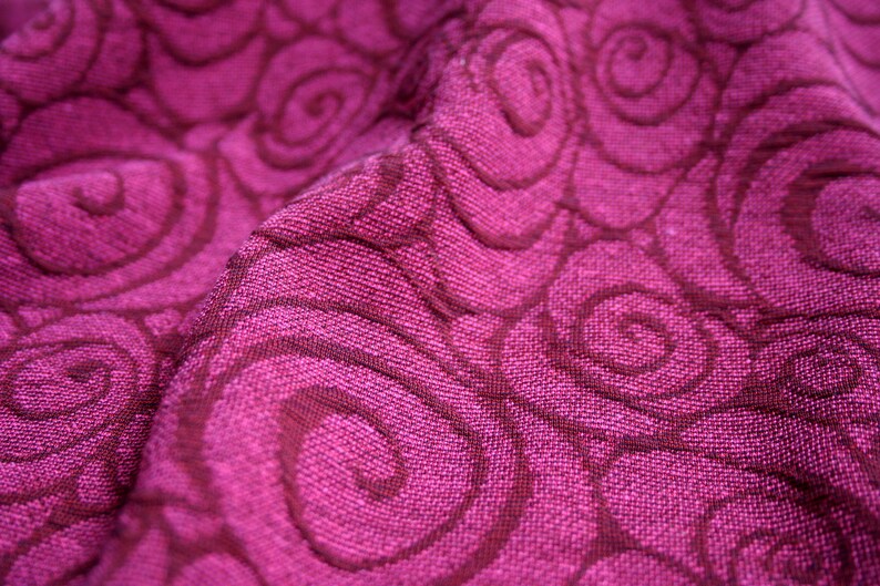 Peut inclure: Gros plan sur un tissu magenta avec un motif de tourbillons r&eacute;p&eacute;t&eacute;s dans une nuance plus fonc&eacute;e de magenta. Le tissu textur&eacute; semble &ecirc;tre tiss&eacute;, avec des fils visibles et un l&eacute;ger &eacute;clat. Les tourbillons cr&eacute;ent un effet de mouvement.