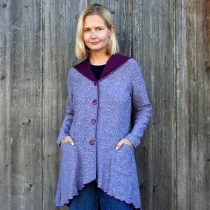 Peut inclure: Un manteau boutonné lavande avec un motif tourbillonnant et un col et une bordure violets foncés. Le manteau a deux poches et est porté sur un haut noir et un jean bleu. Le manteau arrive au genou.