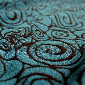 May include: Close-up of a teal fabric with a brown swirl pattern. The fabric is textured and has a soft, woven look.