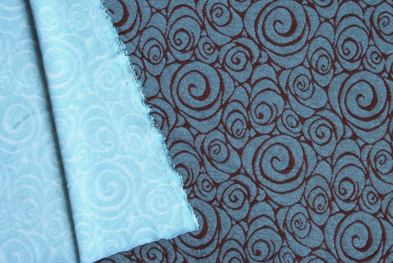 May include: Two pieces of fabric with a swirling pattern. One piece is a light blue fabric with a white swirl pattern. The other piece is a dark blue fabric with a brown swirl pattern.