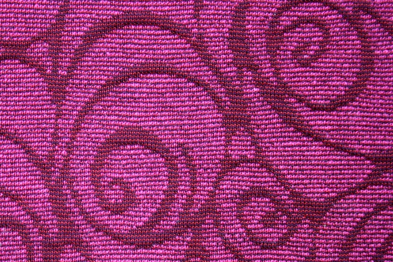 Peut inclure: Gros plan sur un tissu textur&eacute; avec un motif r&eacute;p&eacute;titif de volutes bordeaux fonc&eacute; sur un fond magenta vif. Le tissu a un aspect tiss&eacute;, avec des fils horizontaux et verticaux visibles.