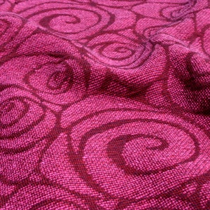 Könnte beinhalten: Nahaufnahme eines strukturierten Stoffes in Magenta- und Dunkelburgundertönen. Der Stoff weist ein sich wiederholendes Muster aus wirbelnden, spiralförmigen Designs auf. Das Gewebe des Stoffes ist sichtbar und verleiht dem Gesamtbild Tiefe und Textur.