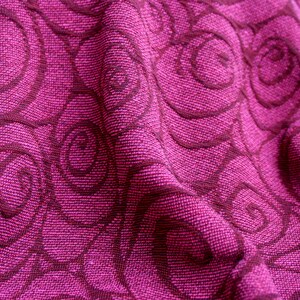 Peut inclure: Gros plan sur un tissu textur&eacute; magenta vif. Le tissu pr&eacute;sente un motif r&eacute;p&eacute;titif de motifs tourbillonnants en forme de rose dans une nuance plus fonc&eacute;e de magenta, cr&eacute;ant un contraste et une profondeur subtils.