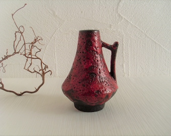 May include: A red and black ceramic vase with a textured surface and a handle. The vase is in a minimalist style.