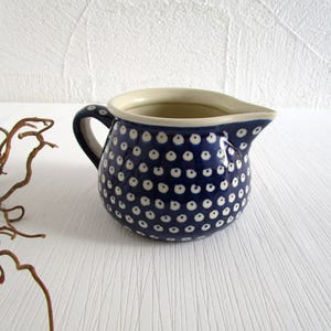 Könnte beinhalten: Ein kleiner, weißer und blauer Keramik-Milchkännchen mit einem Tupfenmuster. Der Milchkännchen hat einen abgerundeten Körper und einen kleinen Ausguss.