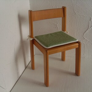 Könnte beinhalten: Ein Holzstuhl mit einem grünen Kissen. Der Stuhl hat ein schlichtes Design mit vier Beinen und einer Rückenlehne.