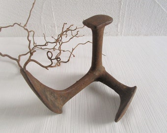 May include: A rusty metal shoe last, a tool used by cobblers to shape and repair shoes. The last is made of cast iron and has a three-pronged base.