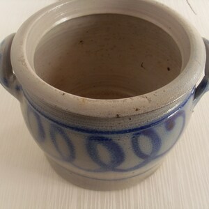 May include: A white ceramic crock with two handles and a blue and white design. The crock has a lid and is decorated with a repeating pattern of blue circles.