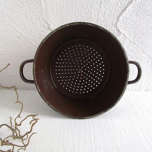 Könnte beinhalten: Ein Vintage-Metallsieb in Braun mit zwei Griffen. Das Sieb hat einen perforierten Boden und einen dunkelbraunen Innenraum. Die Außenseite ist dunkler braun mit einem leicht gealterten Aussehen. Das Sieb dient zum Ablassen von Flüssigkeiten aus Lebensmitteln.