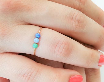 May include: A delicate gold ring with three small beads in shades of blue and green.