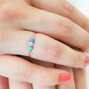 Könnte beinhalten: Ein zarter Goldring mit drei kleinen Perlen in Blautönen und Grün.