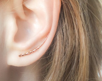 May include: A rose gold ear cuff with a hammered texture. The cuff is curved and sits on the upper part of the ear.