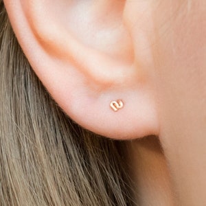 Könnte beinhalten: Nahaufnahme eines Ohrs mit einem kleinen goldenen Ohrstecker. Der Ohrstecker ist in einem schlichten, minimalistischen Design gehalten.