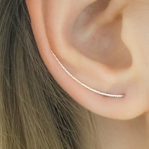 Könnte beinhalten: Ein silberner Ohrring mit einem geschwungenen Design. Der Ohrring wird im oberen Teil des Ohrs getragen.