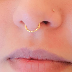 Könnte beinhalten: Nahaufnahme eines Gesichts mit einem goldenen Nasenring. Der Ring ist ein verdrehter Reifen.