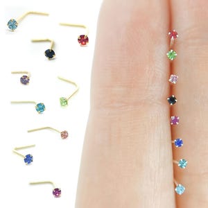 Peut inclure: Un assortiment de piercings de nez avec des strass de différentes couleurs. Les anneaux sont en or et ont une petite forme incurvée. Les strass sont disponibles en couleurs telles que le bleu, le vert, le rouge, le rose et le violet.