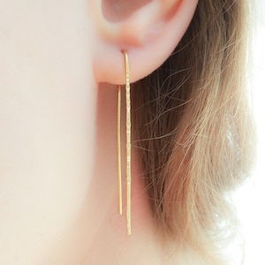 May include: A pair of long, thin gold earrings with a textured finish. The earrings are hanging from the earlobe and are about 2 inches long.