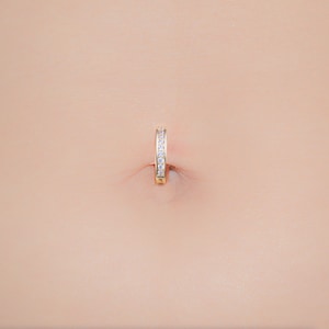 May include: A gold belly button ring with a row of clear cubic zirconia stones.