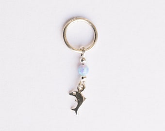 May include: Silver charm with a dolphin and a light blue opal bead. The charm is attached to a silver ring.