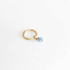 Puede incluir: Un aro de oro para la oreja con una pequeña perla azul iridiscente que cuelga.