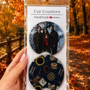 May include: Two circular car coasters in a clear plastic package. The top coaster features a photographic print of three people in leather jackets. The bottom coaster has a dark blue pattern with icons including a teddy bear, pancakes, and a sun.