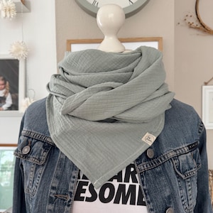 Könnte beinhalten: Hellgrüner, dreieckiger Schal aus weichem, strukturiertem Stoff. Der Schal ist um den Hals einer Schaufensterpuppe drapiert, über einer Jeansjacke und einem weißen T-Shirt mit dem Aufdruck "AWESOME". Ein kleines Etikett ist auf den Schal genäht.