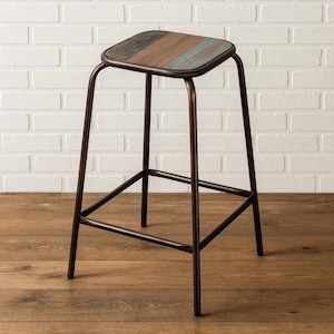 Op de afbeelding: Een rustieke barkruk met een vierkante zitting en een metalen frame. De zitting is gemaakt van hout met een verweerde afwerking in bruin, blauw en grijs. Het donkerbruine metalen frame heeft een voetensteun.