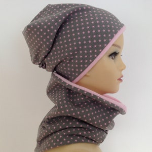 Op de afbeelding: Grijze beanie en bijpassende nekwarmer met een roze sterrenpatroon.