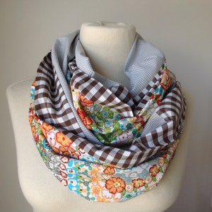 Könnte beinhalten: Ein brauner und weißer Gingham-Muster-Infinity-Schal mit einem Blumendruck auf einer Seite. Der Schal ist aus Baumwollstoff und ein tolles Accessoire für jedes Outfit.