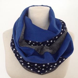 Può includere: Una sciarpa infinita blu e grigia con un motivo a stelle bianche. La sciarpa è piegata ed esposta su un manichino bianco.
