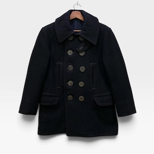 May include: A dark navy blue double-breasted pea coat featuring a wide collar, long sleeves, and eight large round buttons arranged in two vertical rows. The coat includes two vertical slit pockets at the chest and two flap pockets at the waist.