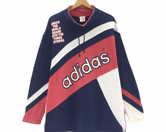 May include: A blue, red, and white Adidas sweatshirt with a large Adidas logo on the front. The sweatshirt has a drawstring hood and the text "Adidas the world brand with the three stripes" on the left side.