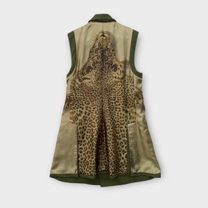 Puede incluir: Un chaleco sin mangas en verde oliva con un diseño de estampado de leopardo en la espalda. El chaleco tiene cuello y bolsillos. El estampado de leopardo es marrón y negro, y el chaleco está hecho de un material satinado.